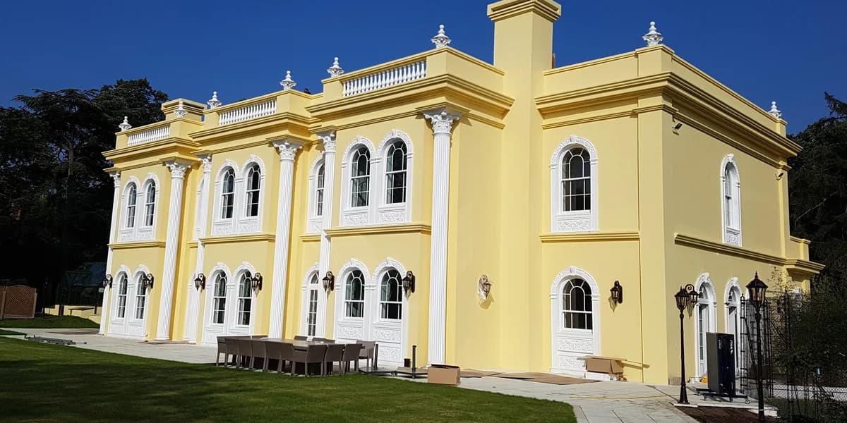 Full-height fluted columns and roofline balustrades on a yellow Surrey residence