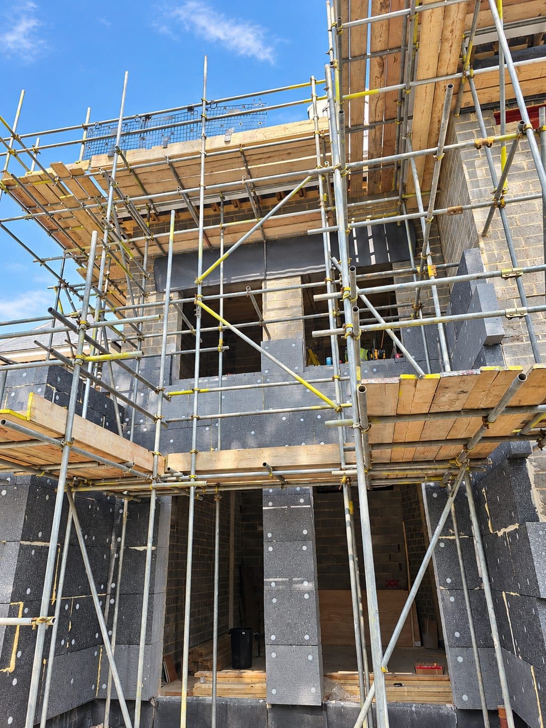 Grey graphite insulation boards with fixings on the walls of a house behind scaffolding