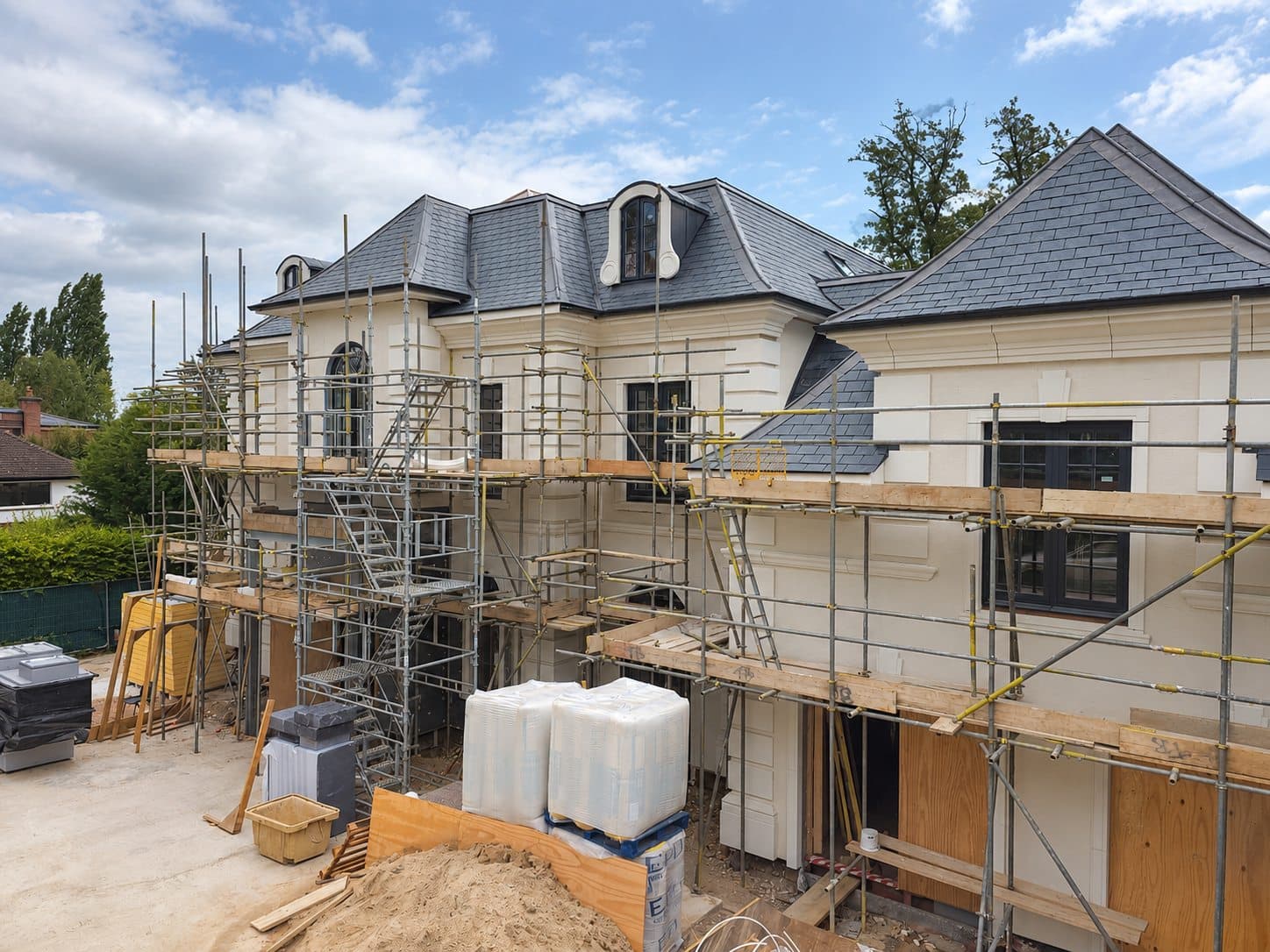 Large house with cream render over the insulation, behind scaffolding near completion