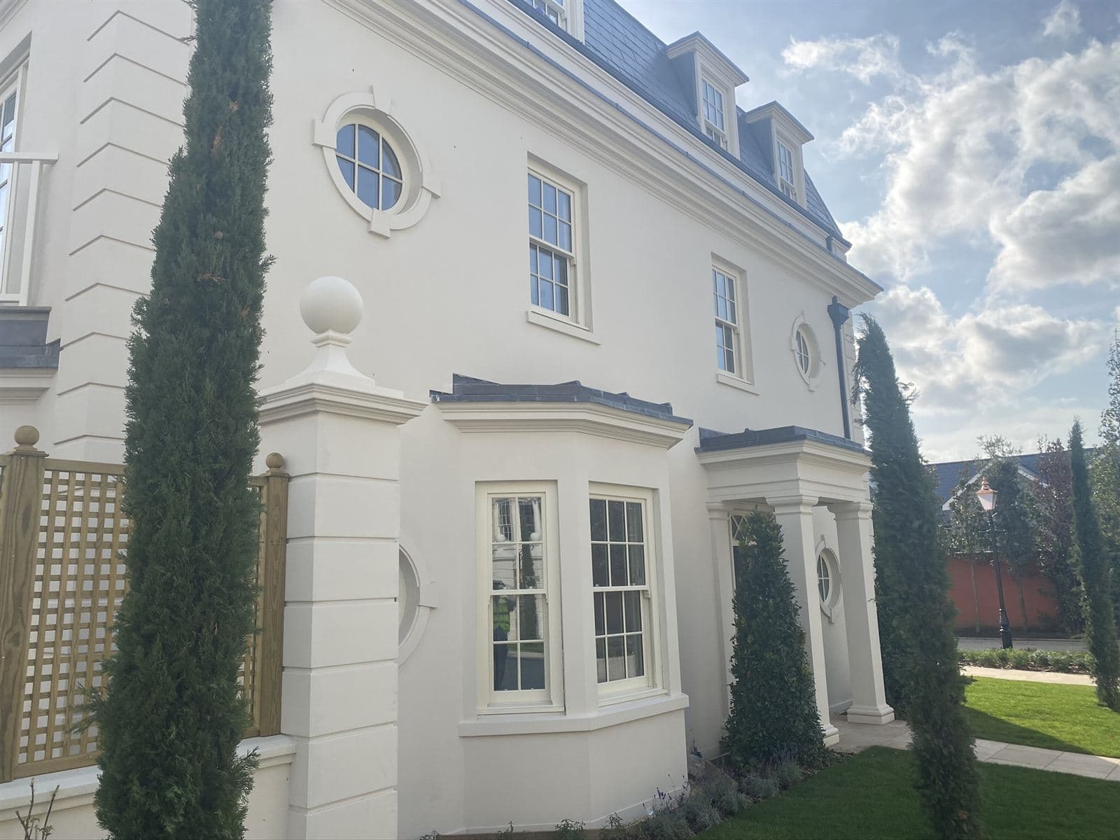 Cream rendered house with a bay window, columned porch, round windows, quoins and a ball-topped pier