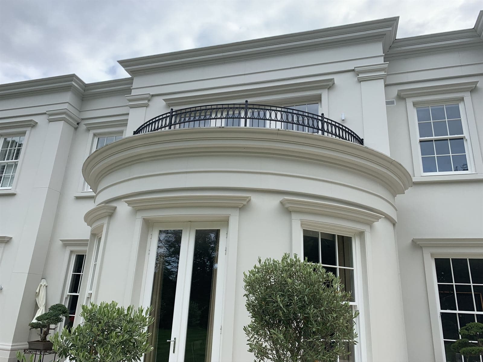 White rendered curved bay with a projecting cornice, window heads and a black balcony railing