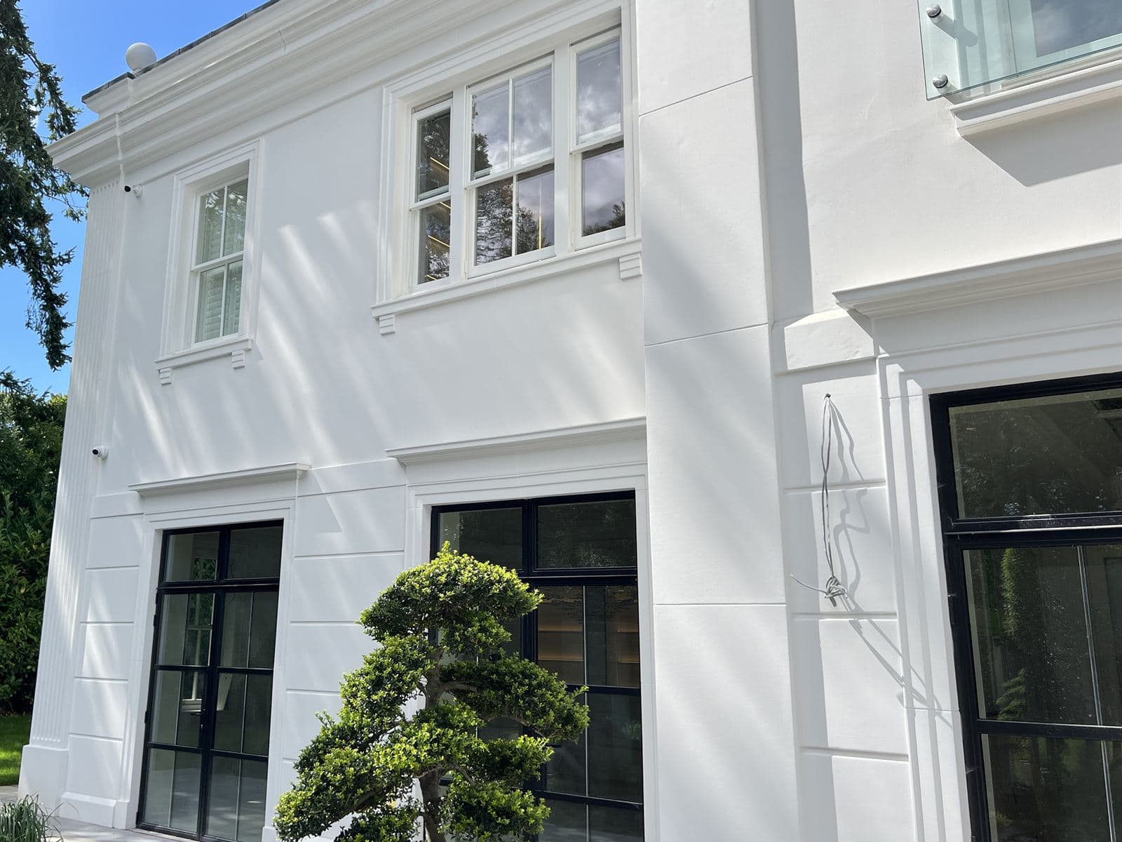Close view of smooth white render with window surrounds, cills, a string band and black-framed doors
