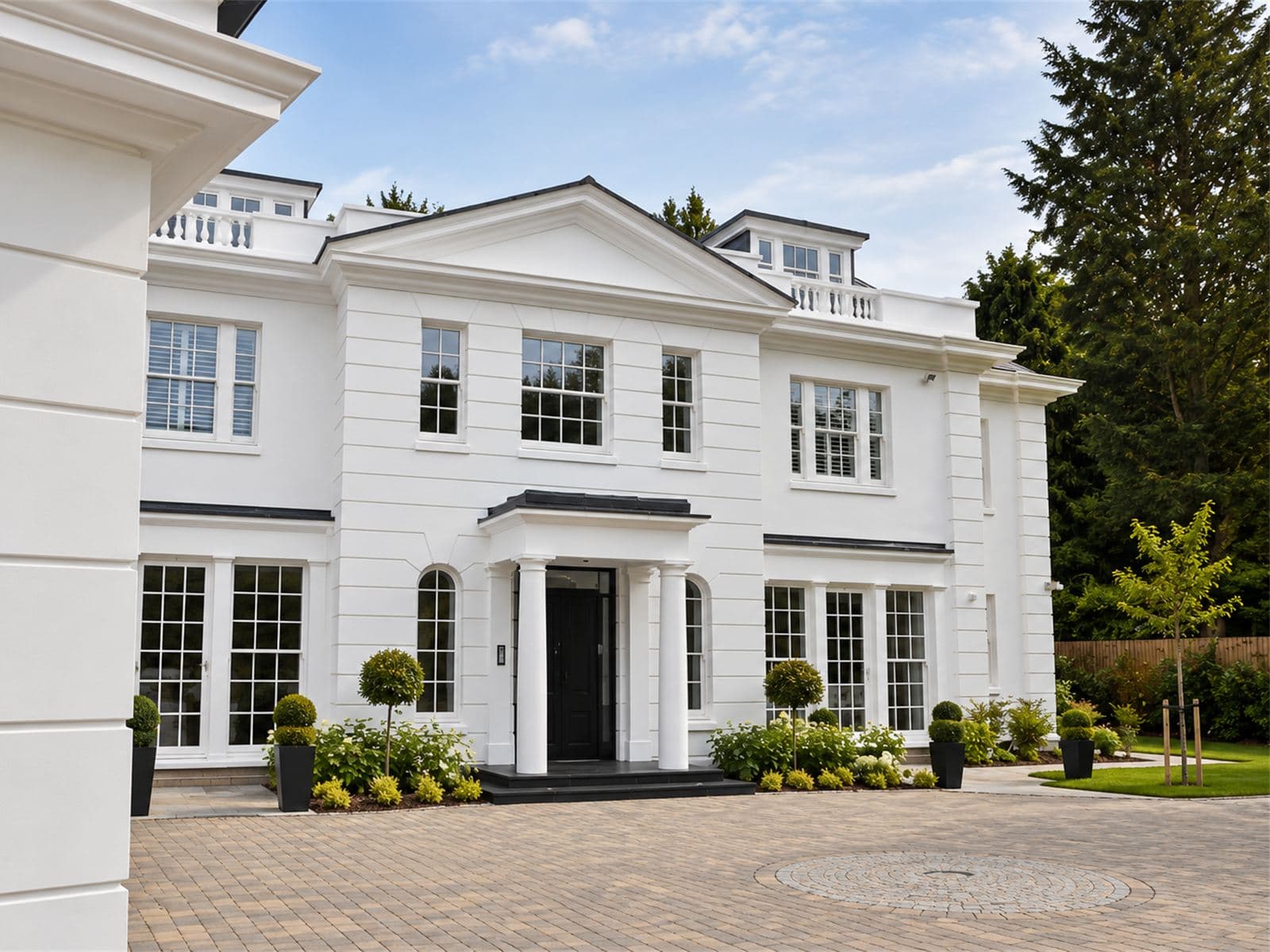 White rendered house with a central pediment, columned porch, balustrades and sash windows