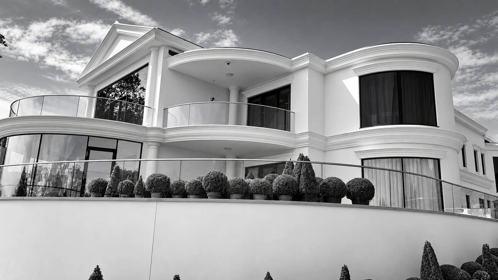 Garden elevation of a white classical house in Swansea with curved cornices, curved string bands, a pediment, columns and glass balustrades.